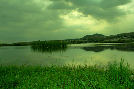 Landscape of a lake with green grass and mountains in the backgroundの写真素材