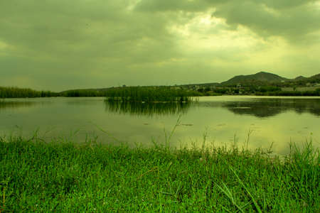 Landscape view of a lake with green grass and mountains in the backgroundの写真素材