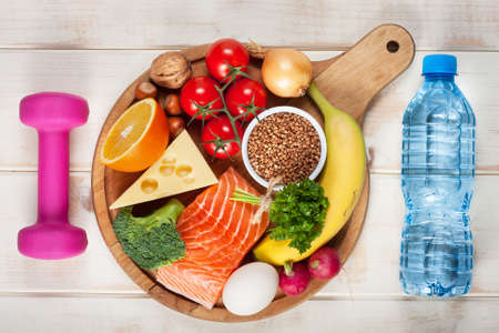 Healthy lifestyle concept. Dumbbell, bottle of water and healthy organic food on wooden table