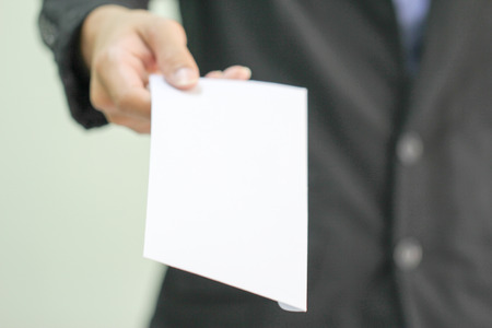 A businessman handing in a blank envelope  focus on hand holding envelope, other out of focus の写真素材