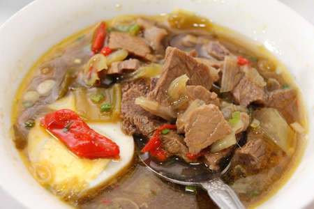 Rawon or Indonesian beef black soup, served in white bowl with boiled eggの写真素材