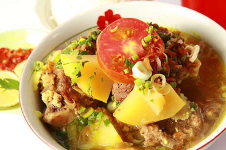 Indonesian oxtail soup or sop buntut, served in white bowl with potatoe and slice of tomatoの写真素材
