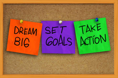 The words Dream Big, Set Goals, Take Action written on sticky colored paper over cork boardの写真素材