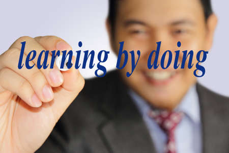 Business concept image of a happy smiling successful businessman writing Learning by Doing on virtual screenの写真素材