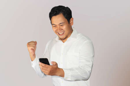 Happy smiling Asian businessman with success gesture after receiving news from his cell phoneの写真素材