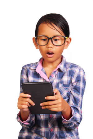 Little girl with glasses shocked while looking her tablet isolated on whiteの写真素材