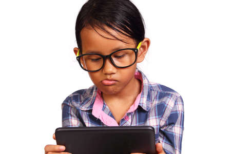 Little girl with glasses seriously playing her tablet isolated on whiteの写真素材
