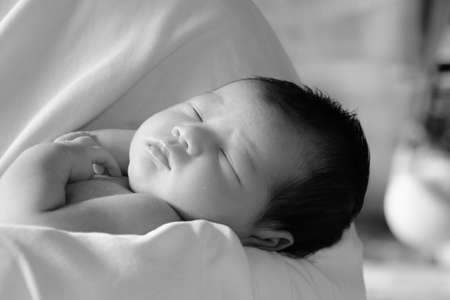 Cute newborn baby girl wrapped in white blanket lying and sleeping in her mom's armの写真素材