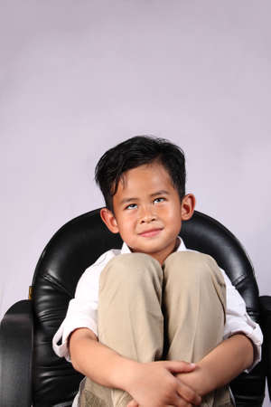 Happy Asian boy smiling and dreaming while sitting on chairの写真素材