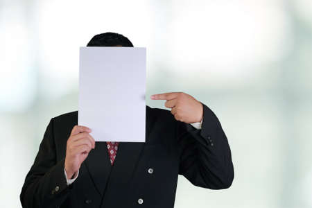 Business concept image of a businessman holding and pointing empty white paper in front of his faceの写真素材