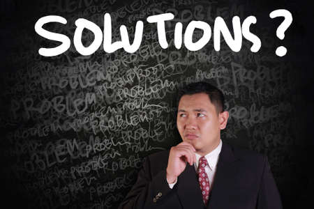 Problems and Solutions Concept, Asian businessman thinking of solutions with problems words on chalk...