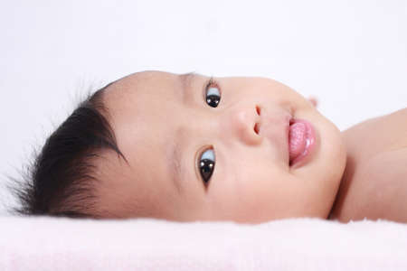 Portrait of cute little Asian baby girl lying down on bed and smiling to the camera and showing her...