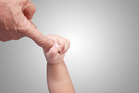 Close up image of baby's hand holding elderly's finger