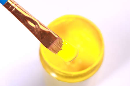 Painting brush with yellow acrylic paint in bottle from above view