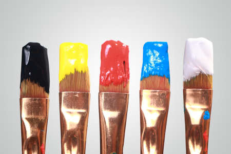 Paint brushes with black, yellow, red, blue and white acrylic paintの写真素材