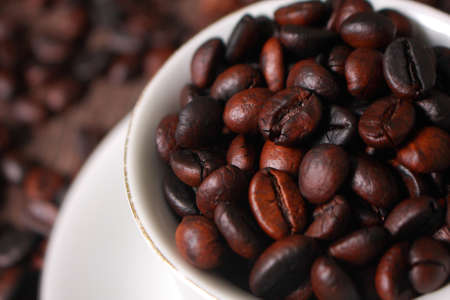 Dark roasted coffee beans in white cup with blurred coffee beans and old wooden texture on backgroundの写真素材