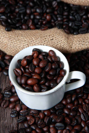 Dark roasted coffee beans in white cup with blurred coffee beans and gunny sack texture on...
