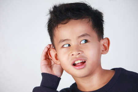 closeup portrait of young Asian boy listening carefully with his hand to ear gesture trying to hear secretly interesting information conversation newsの写真素材