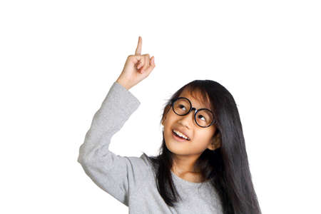 Portrait of beautiful little Asian student girl smiling and raise her pointing finger up get an idea gesture, isolated on whiteの写真素材