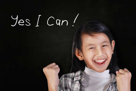 Portrait of happy and smiling cute beautiful Asian girl over blackboard with motivational words Yes I can written on itの写真素材