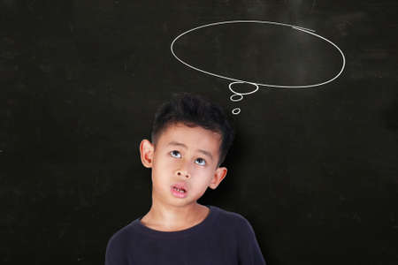 Portrait of Asian little boy looking up and thinking something, over blackboard with empty dreaming...