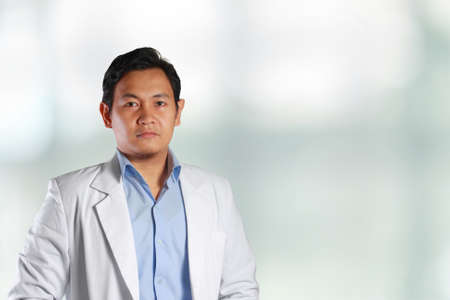 Photo image of a handsome, attractive, confident, successful young Asian male doctor smiling to the front with blurred, out of focus backgroundの写真素材
