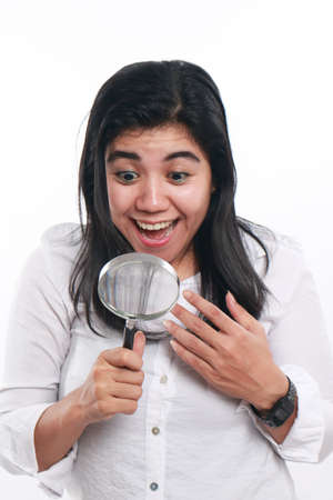 Photo image portrait of a beautiful cute young Asian woman with mole looked very happy and smiling to find something while looking into magnifying glass, close up portrait over white backgroundの写真素材