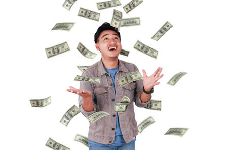 Photo image portrait of a cute young successful Asian male under rain of money, isolated on white