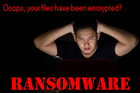 Young man shocked in front of his laptop in the dark to see his files on his computer have been encrypted by ransomware virusの写真素材
