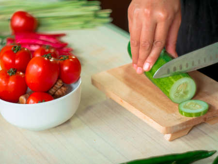 Slicing cucumber to make fresh raw mixed vegetables salad. Healthy vegetarian food mealの写真素材