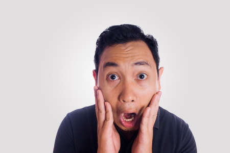 Funny Asian man shocked gesture silly face hands on cheek. Close up face portrait expression