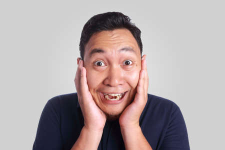 Photo image of funny cute Asian man smiling while hold his cheeks with supporting hands