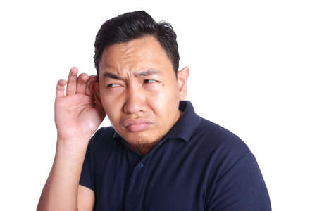 Photo image of funny Asian man put his hand on ear to listen carefully of gossip or whispering, isolated on whiteの写真素材