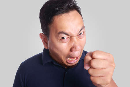 Photo image of funny Asian man showing synical unhappy angry mad punching fighting facial expression