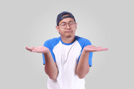 Photo image portrait of a cute funny young Asian man showing something on his open palms, thinking...