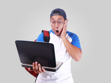 Portrait of young funny Asian student smiling and shocked while looking his laptop