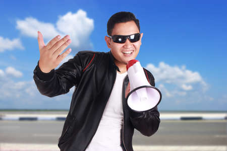 Photo image portrait of funny young Asian man shouting with megaphone, mad yelling screaming crazy supporting motivating conceptの写真素材
