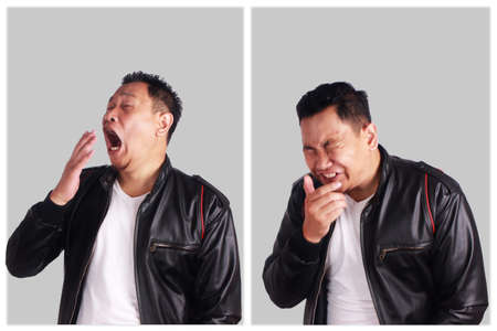 Portrait of funny young Asian man wearing black leather jacket sneezing, over grewy background