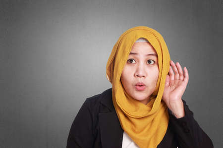 Portrait of young muslim businesswoman hearing gesture, put hand on ear, listening carefullyの写真素材