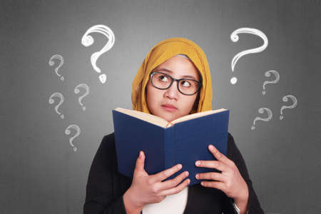 Portrait of young muslim businesswoman wearing hijab reading book and thinking questionsの写真素材