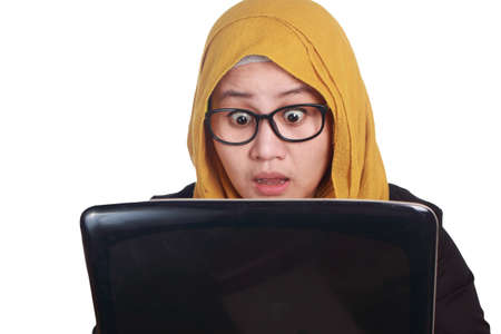 Portrait of muslim businesswoman wearing hijab using laptop with shocked stunned facial expression...