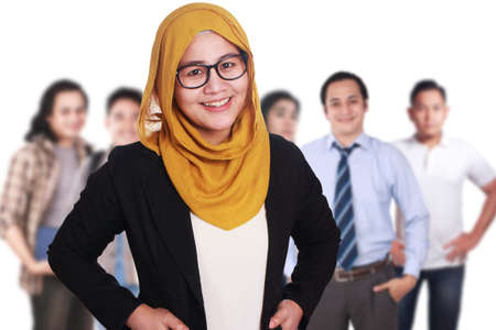 Portrait of muslim businesswoman manager wearing hijab standing smiling in front of creative people staff, leadership concept, focus on foreground の写真素材