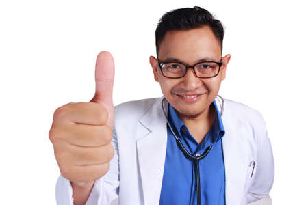 Portrait of young funny Asian male doctor wearing glasses and sthetoscope smiling to camera showing thumb upの写真素材