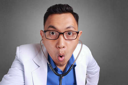 A Young Asian doctor with eyeglass, medical professional in shock with a surprise face, Looking at Cameraの写真素材