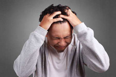 Young Asian man wearing white shirt and gray jacket cried, stressed expression. Background on gray....
