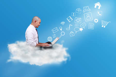 Bald Asian businessman working typing on his laptop while sitting over white cloud on blue sky....