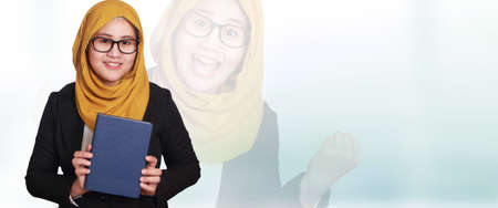 Asian muslimah businesswoman wearing glasses and suit holding a book, smiling expression. Background, web bannerの写真素材