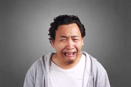 Young Asian man wearing white shirt and gray jacket crying expression. Background on gray. Close up head and shouldersの写真素材