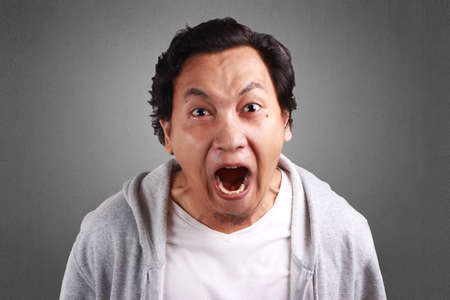 Young Asian man wearing a white shirt and grey jacket shouting because of anger.の写真素材