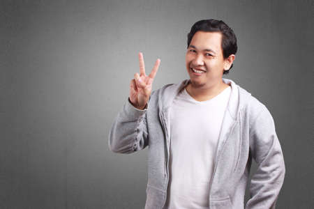 Young Asian man wearing white shirt and gray jacket showing number two sign. Close up body portrait